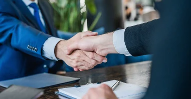 Two businessmen in suits shake hands over a wooden table, symbolizing a successful deal or partnership.