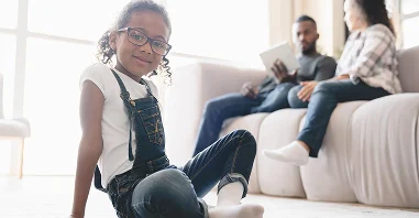 A child in denim overalls sits on the floor, while two adults discuss custody on a couch.