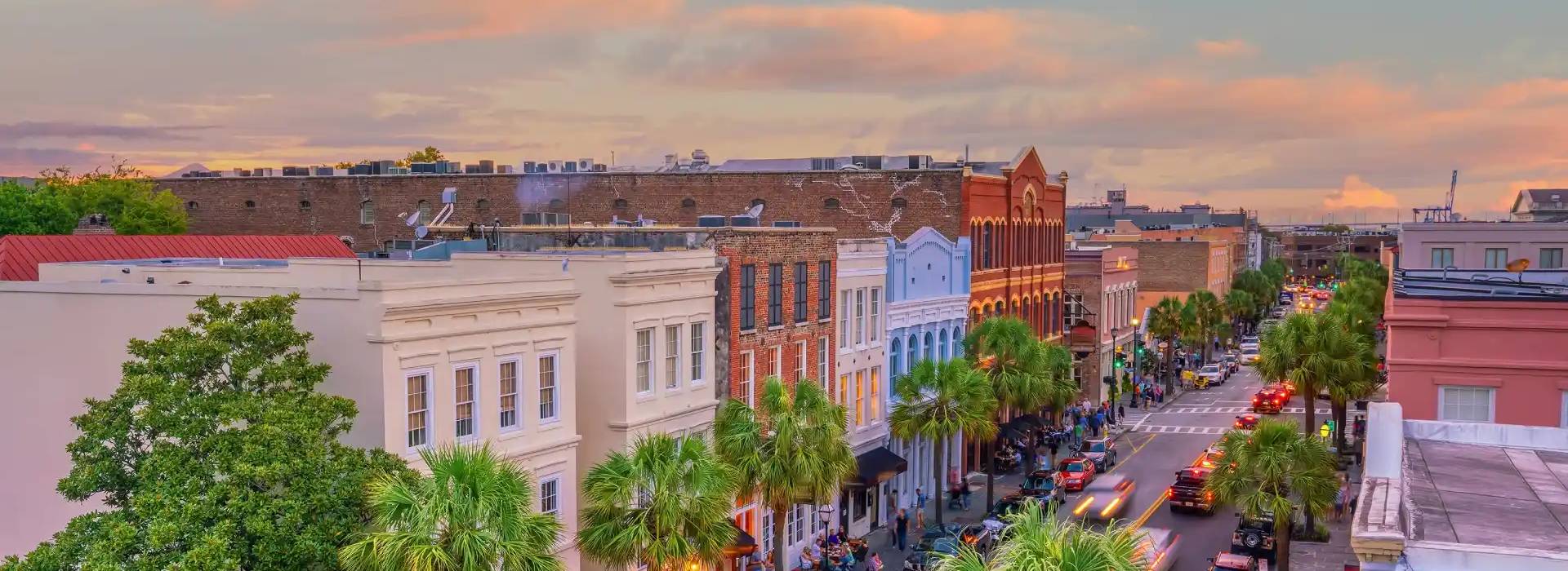 A vibrant street lined with palm trees and historic buildings, bustling with traffic and people under a pastel sunset sky.